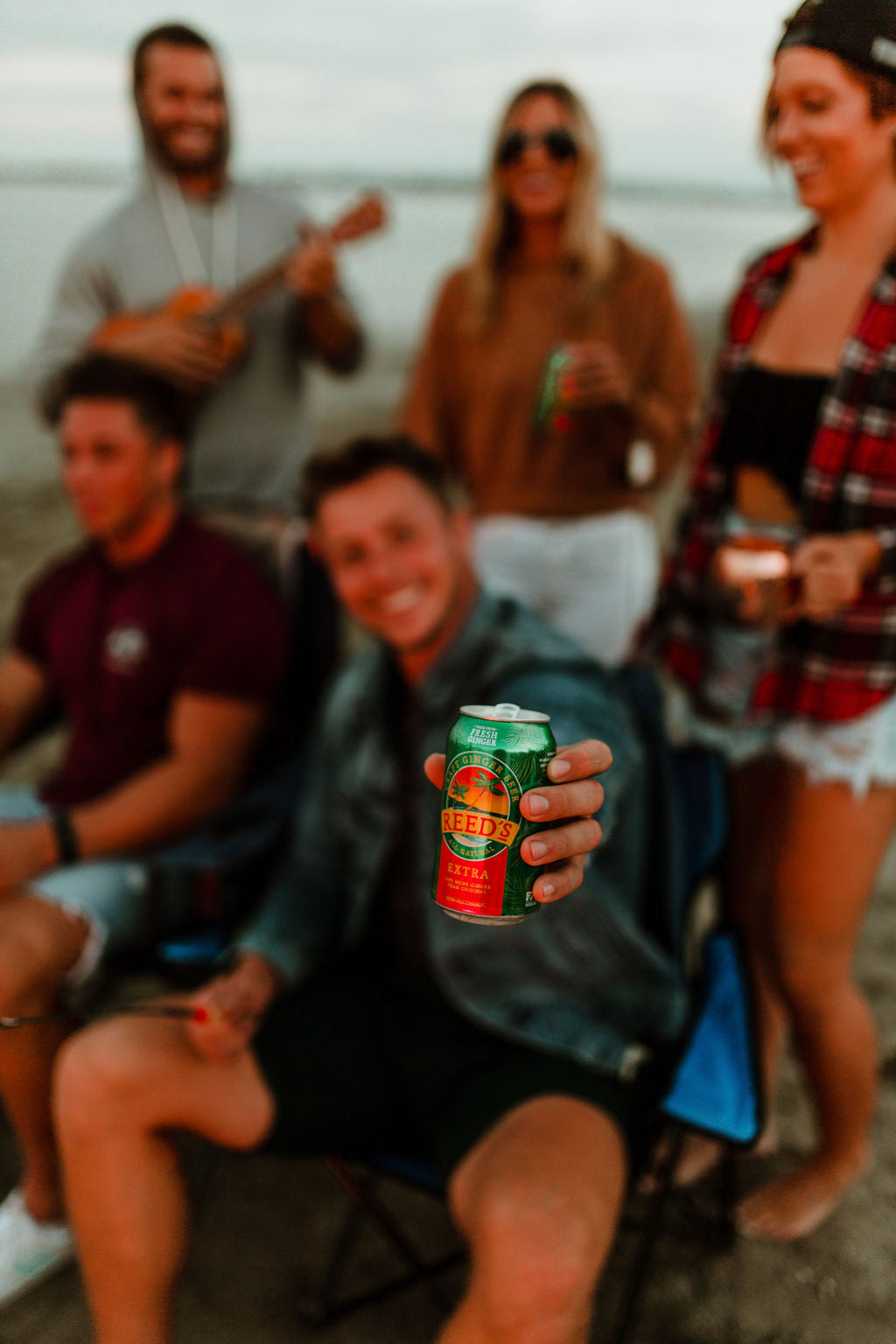 A guy holding a can of Reed's Extra Ginger Beer surrounded by other people.