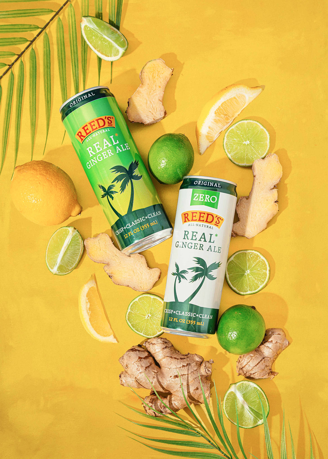 A can of Reed's Real Ginger Ale and Reed's Zero Sugar Ginger ale on a yellow background surrounded by ginger, lemons, leaves, and limes.