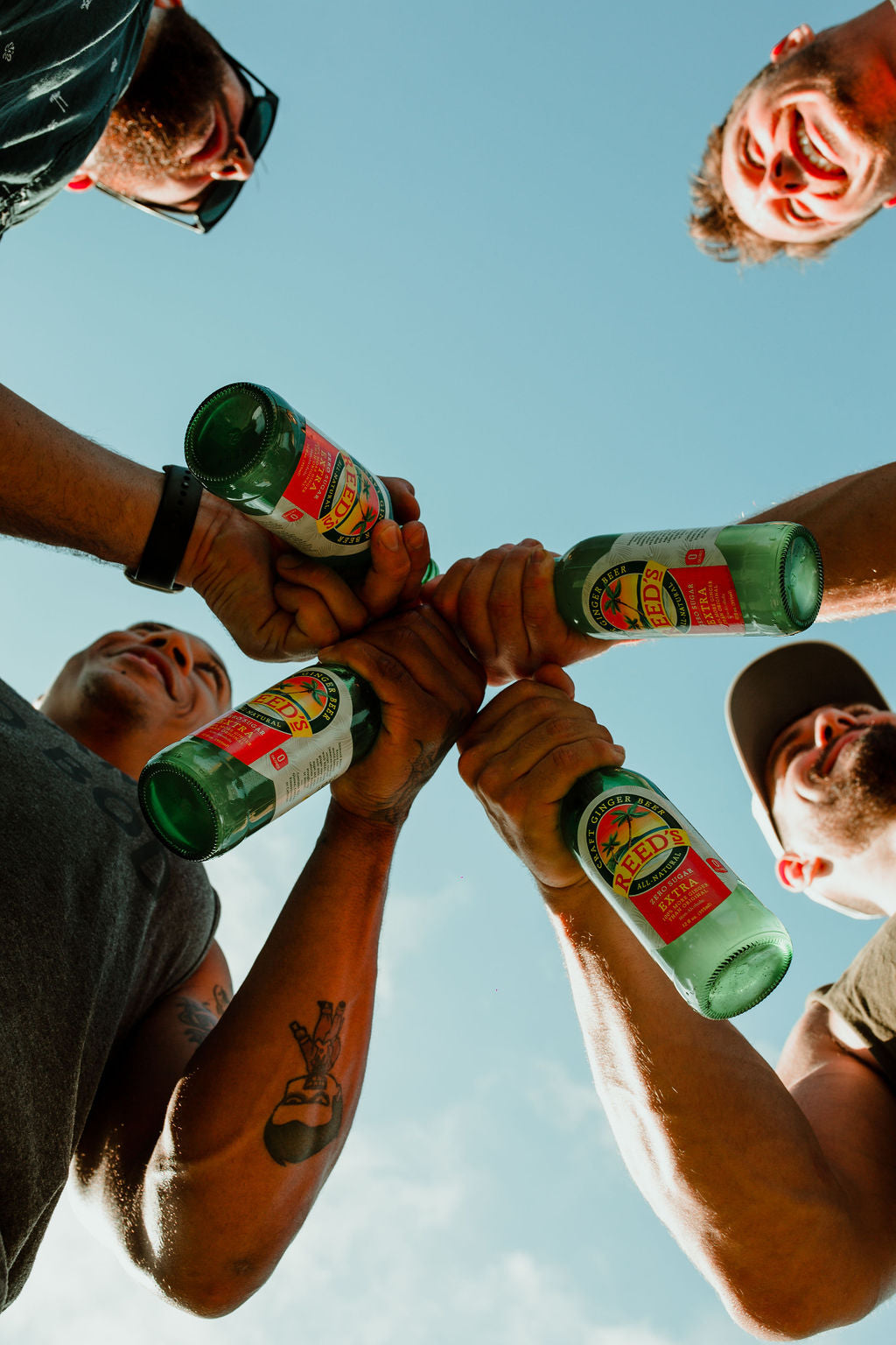 Four men holding glass bottles of Reed's Zero Sugar Extra Ginger Beer.