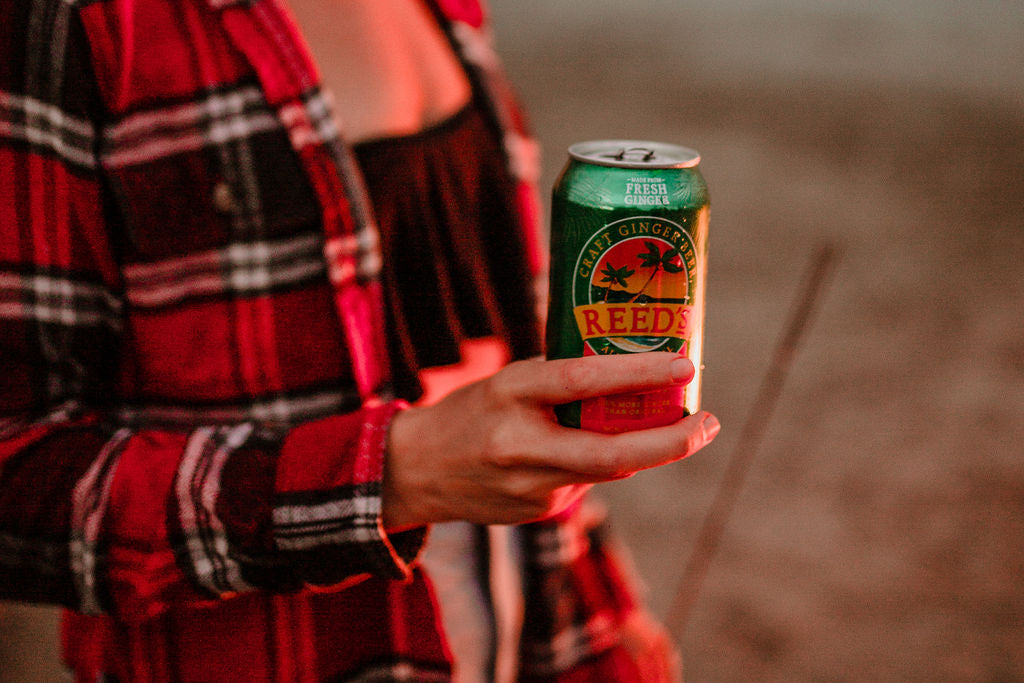 A girl holding a can of Reed's Extra Ginger Beer.