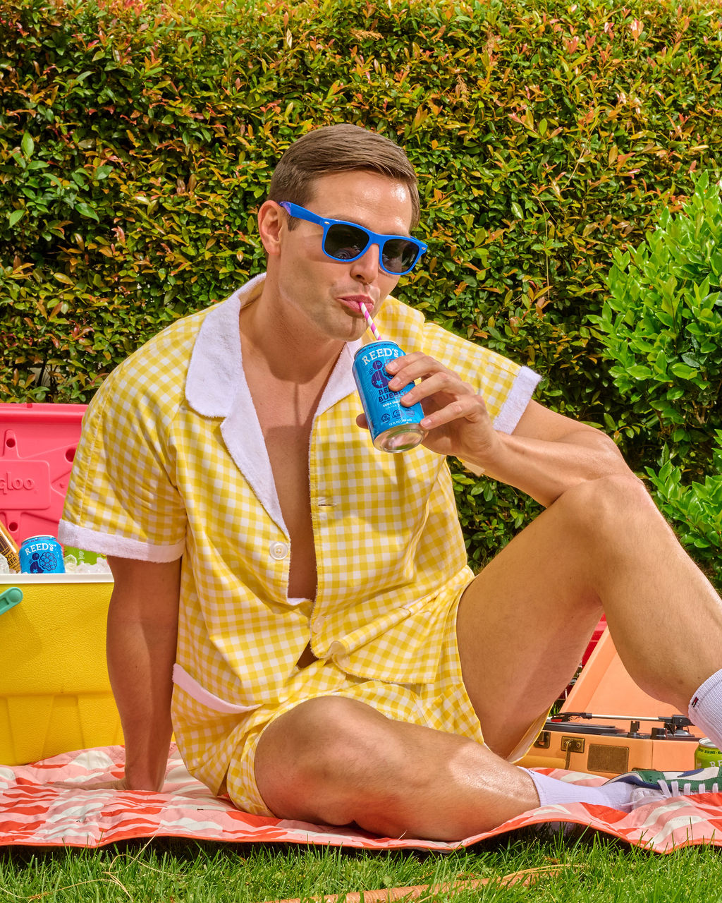 man sitting on picnic blanket drinking reeds new smart soda berry bubbly flavor on a nice day in the sun