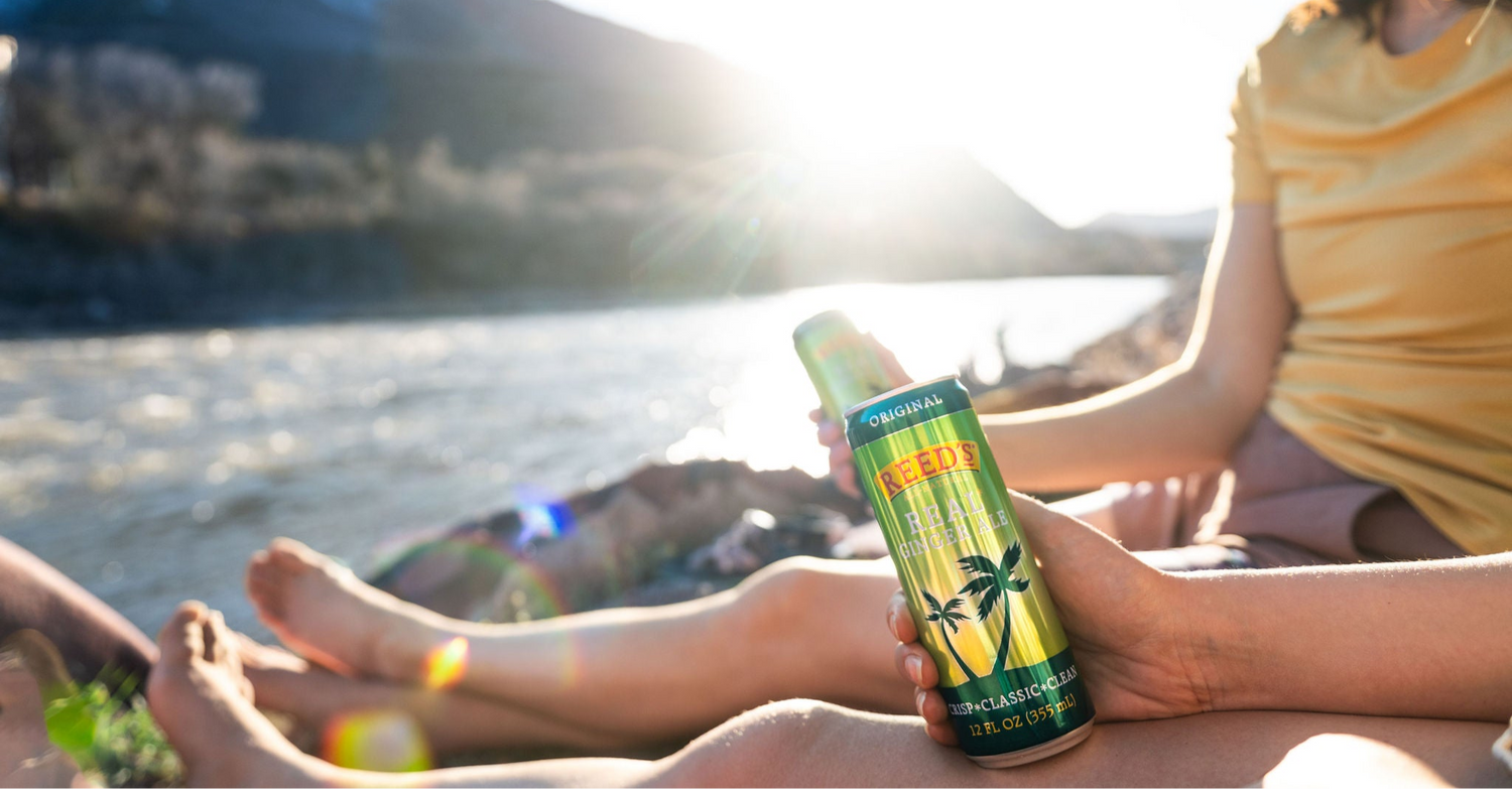 People drinking Reed's Real Ginger Ale next to a body of water.